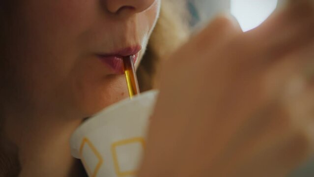 A young woman enjoys a cool drink at a fast food street eatery, the taste of cola conveying the pleasure on her face as she drinks through a straw
