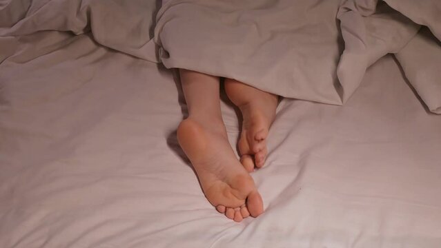 female legs and toes itch and scabies in night in bed on a sheet under a blanket. Woman girl with bare feet foot with fungus under stress sleeps on bed in a bedroom at night in a home