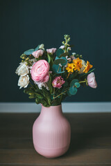 A beautiful bouquet of assorted flowers placed in a pink vase against a dark background