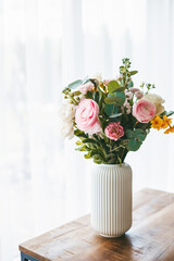 A stunning bouquet of flowers in various hues and types fills a ribbed white vase, standing on a wooden table