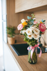 A stunning bouquet of assorted flowers in a clear glass vase with a pink ribbon, set against the backdrop of a contemporary kitchen