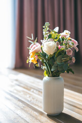 A charming bouquet with an assortment of white roses, pink ranunculus, and yellow blossoms, arranged in a white ribbed vase
