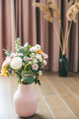 Assorted flowers in a textured pink vase stand out against elegant pink curtains and dried plants in a black vase