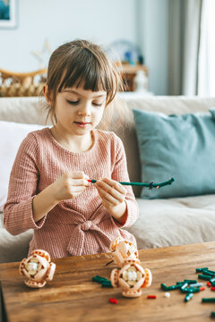 A cute little girl is fully immersed in her imaginative play, arranging small colorful construction pieces, sitting on a sofa in a living-room