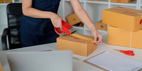 Woman use scotch tape to attach parcel boxes to prepare goods for the process of packaging at home,...