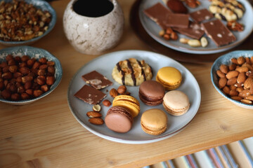 Cup of tea or coffee, cookies, macaroons, chocolate, various nuts and cocoa powder on wooden table. Selective focus.