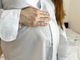 Pregnant girl in a white shirt holds her hand on her stomach. International Day of the Midwife. Mothers Day. International Day of Families. Lazy Mom Day