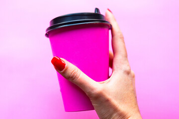 Womanâ€™s hand holds take away coffee cup over pink background. Copy space for the text