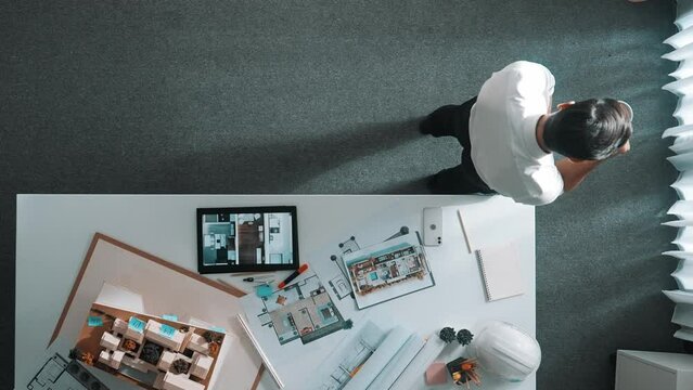 Top view of engineer drink coffee and thinking about house plan at meeting table with equipment and safety helmet scatter around. Aerial view of stressful manager walking and standing. Alimentation.