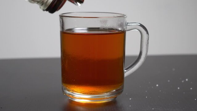 Pouring sugar into a glass cup with a black tea. Stirring sugar with a spoon.