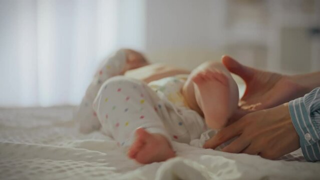 A young tired mother dresses her baby in baby clothes on the changing table. An active child kicks his legs and does not want to put on clothes. The process of dressing a child in children's clothing