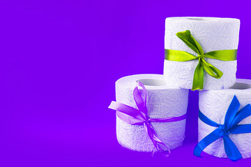 toilet paper rolls wrapped in gift bows on bright purple background. Covid19 concept. Copy space for the text