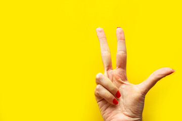 Woman's hand shows the victory gesture over bright yellow background. Minimal concept. Copy space for the text