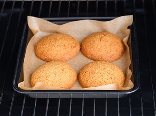 Four oatmeal cookies in a baked tray in an oven.