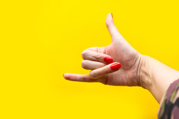 Closeup view of female hand forming gesture call me. Isolated on bright yellow background. Copy space for the text