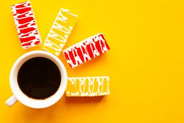 Color glazed cakes and coffee cup on bright yellow background. Top view. Copy space for the text
