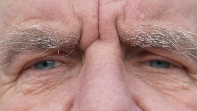 Face of sad elderly man with tears in his blue eyes. Retired man with deep wrinkles on face looks hopefully at camera. Close up macro view. Grey eyebrows