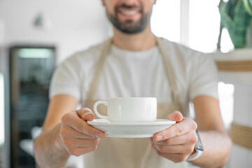 Closeup of barista offering a coffee cup. Coffee shop owner serving coffee. Cropped photo of decaf...