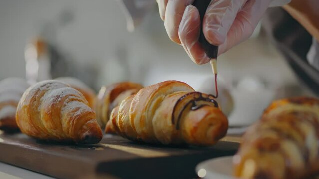 Dough. Master pastry chef pours fresh chocolate over a croissant in a production kitchen. An experienced man pours dark chocolate over baked goods and masters new recipes for baking, assorted