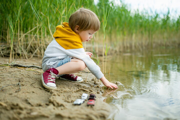 Cute little boy playing by a lake or river on hot summer day. Adorable child having fun outdoors during summer vacations. - 793870723