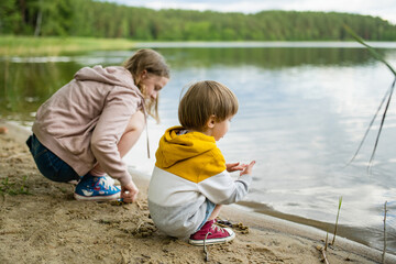 Cute little boy and his sister playing by a lake or river on hot summer day. Adorable child having fun outdoors during summer vacations. - 793870731