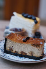 A piece of espresso macadamia cheese cake topped with coffee beans on the plate with blur of blueberry crepe cake.