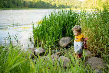 Cute little boy with a backpack having fun outdoors on sunny summer day. Child exploring nature. Kid going on a trip. - 793872357