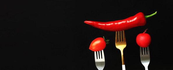 Fresh vegetables on forks, black background. Hot red pepper, tomato and radish on a dark background. Healthy eating concept. Diet
