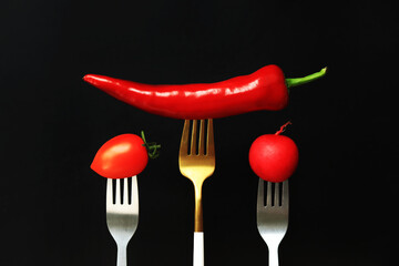 Fresh vegetables on forks, black background. Hot red pepper, tomato and radish on a dark background. Healthy eating concept. Diet