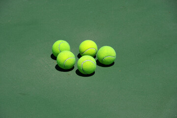 Five yellow tennis balls on a hard surface green tennis court - obrazy, fototapety, plakaty
