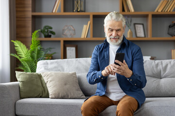 Senior man using smartphone on living room couch