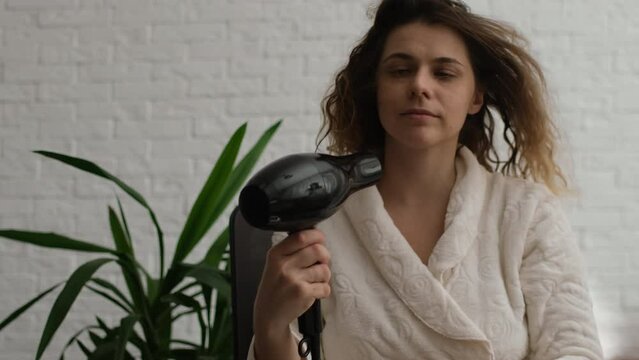 Woman dries her hair with a hair dryer after taking a bath