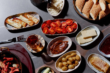 A sumptuous Turkish lunch, the menu of which presents a symphony of flavors. The menu includes bread, cheeses, sliced fresh fruits, pickled vegetables, snacks, hummus. Turkish tea in bowls.