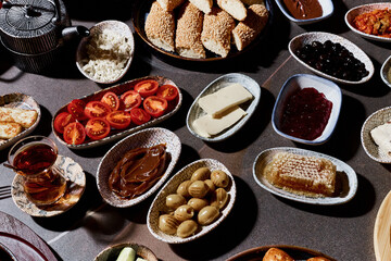 A sumptuous Turkish lunch, the menu of which presents a symphony of flavors. The menu includes bread, cheeses, sliced fresh fruits, pickled vegetables, snacks, hummus. Turkish tea in bowls.