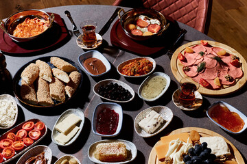 A sumptuous Turkish lunch, the menu of which presents a symphony of flavors. The menu includes bread, cheeses, sliced fresh fruits, pickled vegetables, snacks, hummus. Turkish tea in bowls.