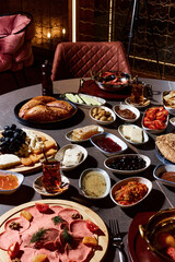 A sumptuous Turkish lunch, the menu of which presents a symphony of flavors. The menu includes bread, cheeses, sliced fresh fruits, pickled vegetables, snacks, hummus. Turkish tea in bowls.