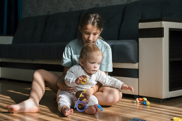 Baby playing on floor with educational toys with sister teen