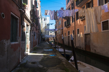 Uno stretto canale di Venezia con dei panni stesi ad asciugare e illuminato da un raggio di sole - Powered by Adobe