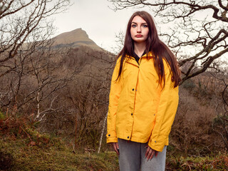 Young teenager girl in yellow jacket on a walk in a dense forest. Travel and tourism concept....