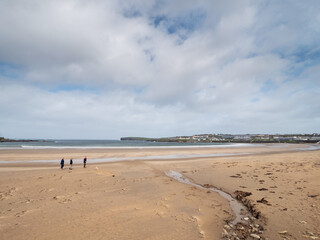 Stream flows into ocean. Kilkee beach, county Clare, Ireland. Cloudy sky. Group of people walking by.