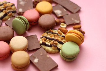Pastel macarons, almond chocolate, peanut butter cookies and various nuts on bright pink background. Selective focus.