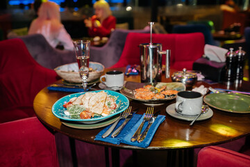 A table with a blue plate of salad and a cup of coffee. The table is set with silverware and a few cups. Scene is casual and inviting, as it is a restaurant setting with people enjoying their meals.