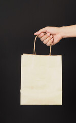Hand is hold brown shopping bag on black background.
