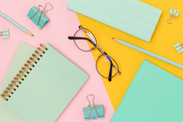 Mint colored school supplies and eyeglasses on a pink and yellow background.