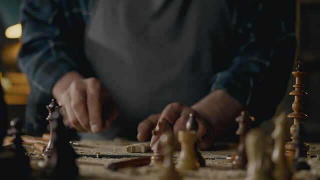 Carpenter. A workshop worker holds a chess piece in his hands and looks at the result. In slow motion, an experienced woodworker making a chess set. Working at a table in a woodworking shop, carpentry