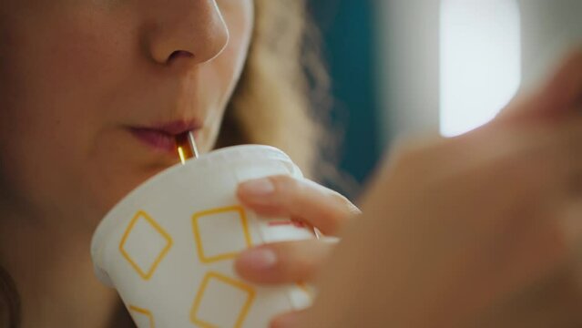 At a table in an authentic cafe, a young girl enjoys sips of a cold drink, her face lit up with pleasure with every sip of cola through a straw