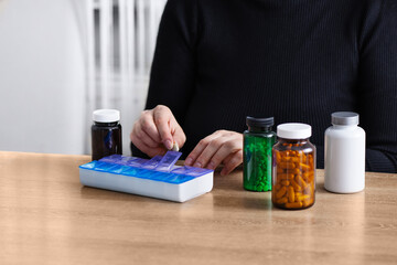 Female putting prescription pills and vitamins in a daily pill box organizer. Sorting nutritional supplements and antibiotics into weekly pills container. - 793907378