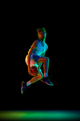Fototapeta premium Slam dunk pose. Young, focused man, basketball player in motion, training against black background in neon light. Concept of sport, competition, active and healthy lifestyle, game