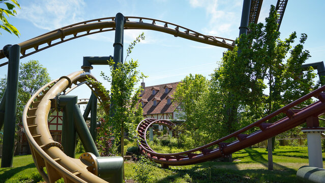 Cleebronn, Germany-May 18.2023:Yellow and red-coloured roller coaster tracks of coasters in"Tripsdrill",crossing near the ground with natur and a half-timbered house,as station, in the background