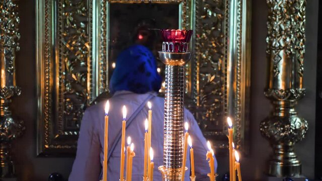 Woman praying to Virgin Mary icon behind candles in orthodox christian church